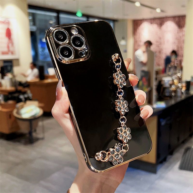 Black phone case with gold-toned frame and blue-toned rhinestone bracelet charm.