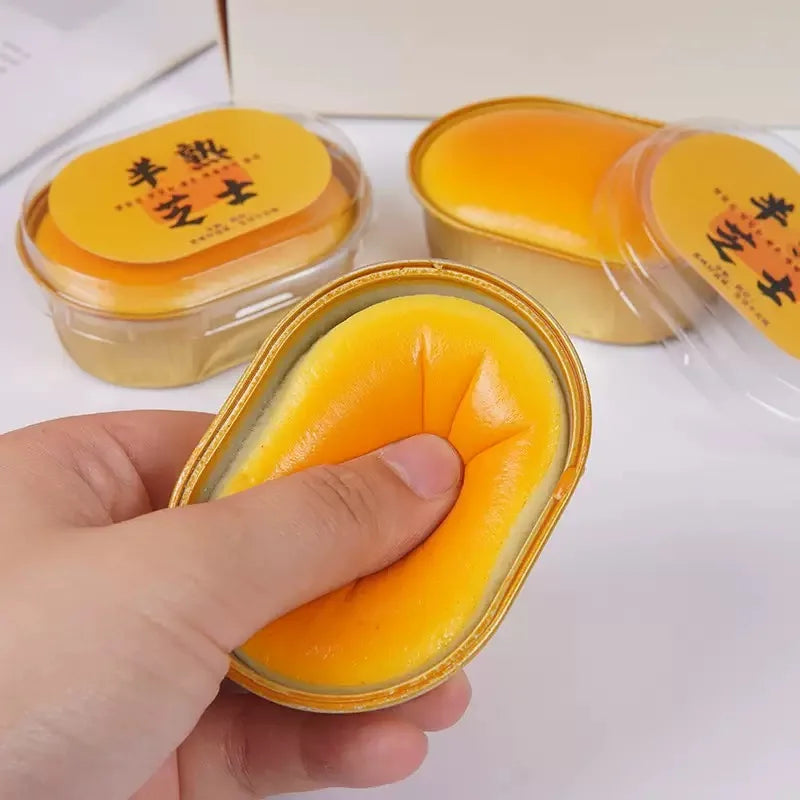 Orange-yellow cheese-shaped squishy toy in clear box, hand pressing